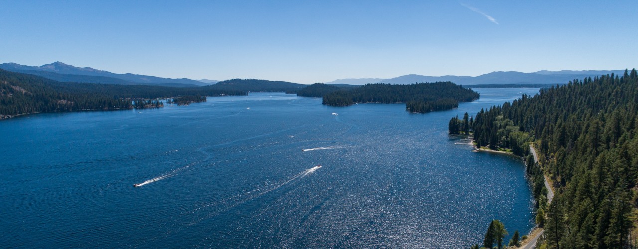 Aerial view of a mountain lake surrounded by trees. There are boats driving across the middle of the water.